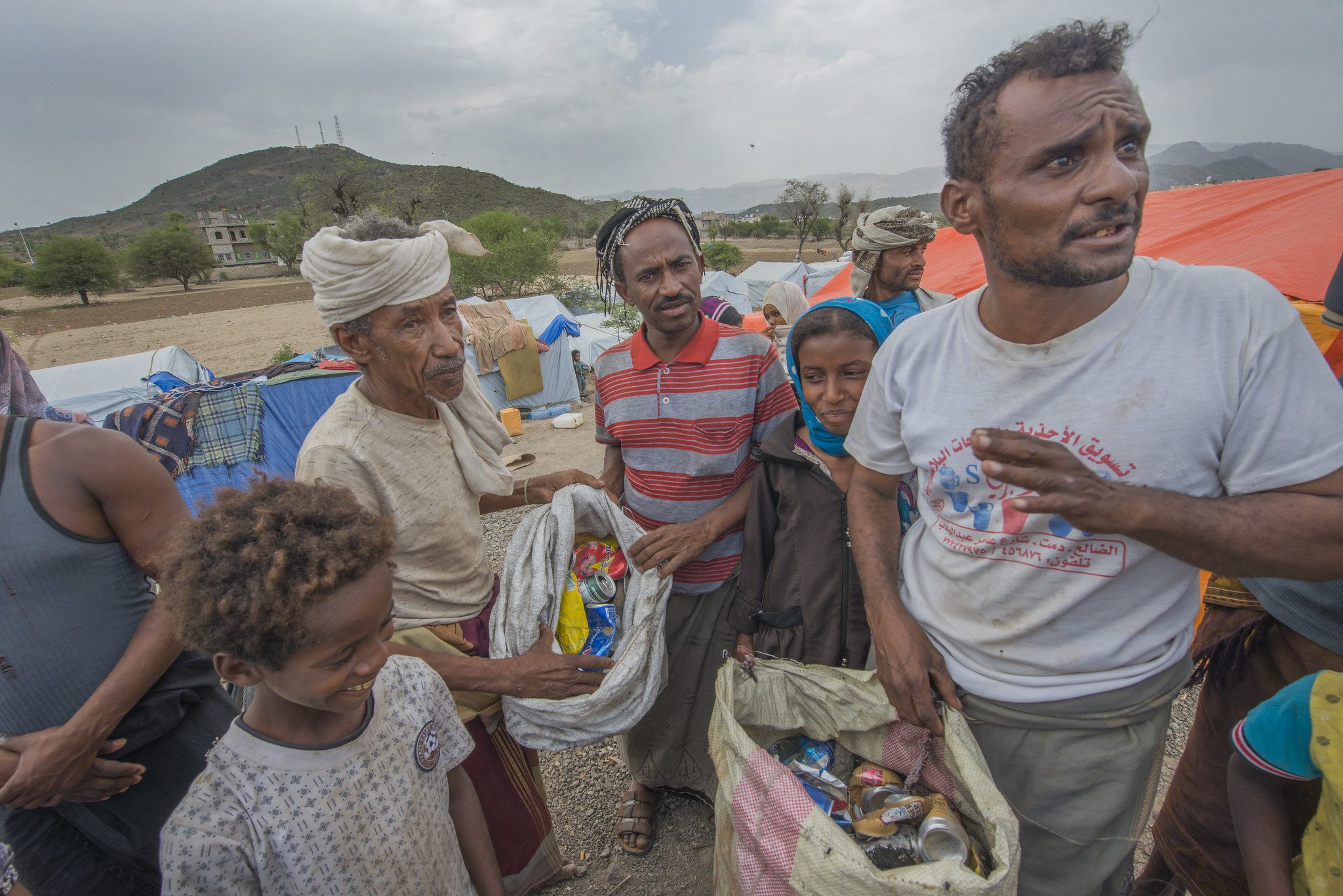 Starving Yemeni community members, group of men and young boys, collect discarded soda cans in a large sack.
